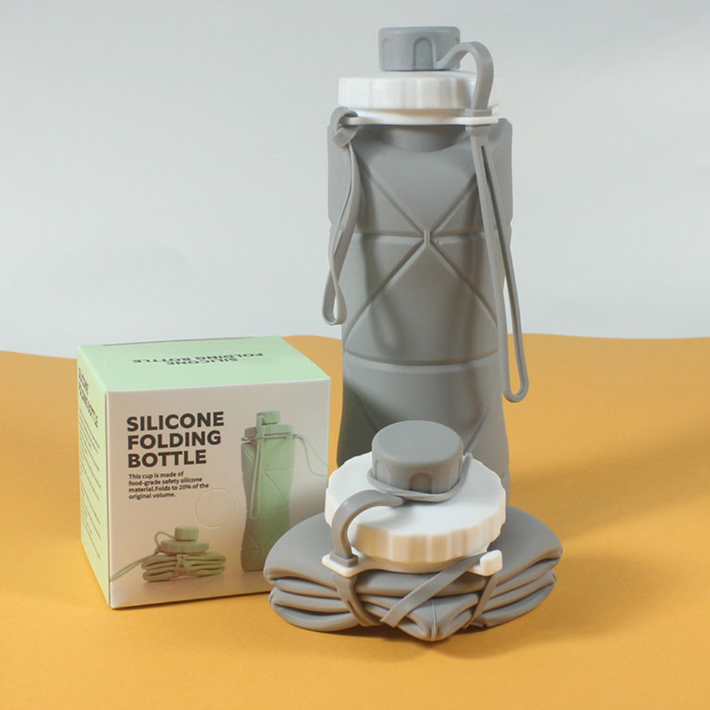 A gray silicone folding water bottle with its box and folded packaging, displayed on a yellow surface against a light gray background.